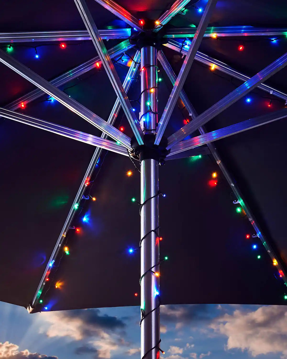 Umbrella with multi colour string lights against a cloudy sky
