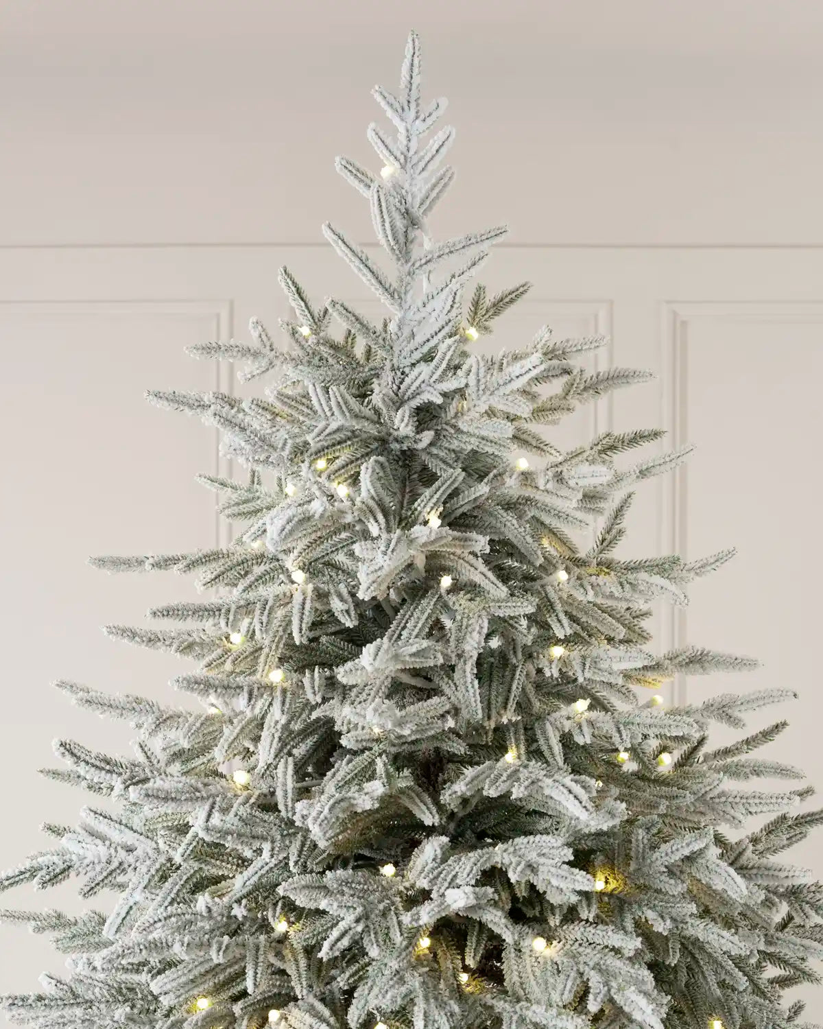 Upper section of a 6.5-foot snow-flocked Grand Duchess Christmas tree decorated with warm white lights