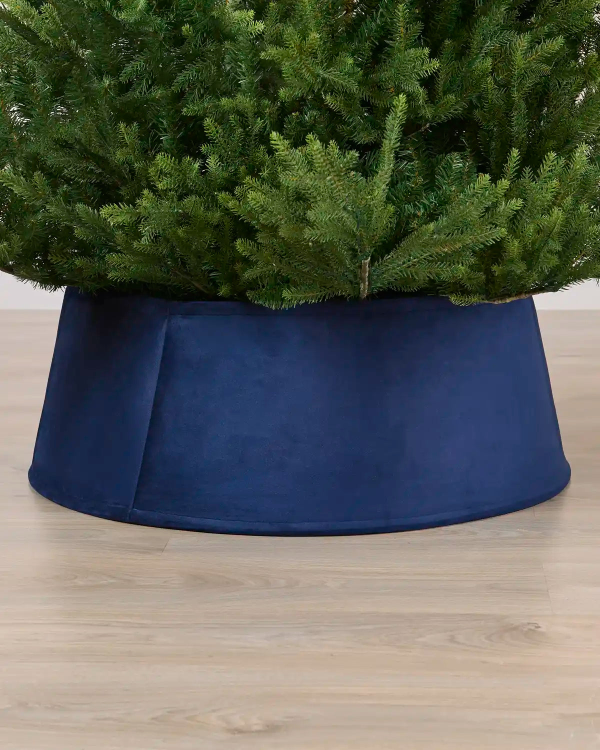 Velvet Navy tree collar around the base of a green Christmas tree placed on a light brown wooden floor
