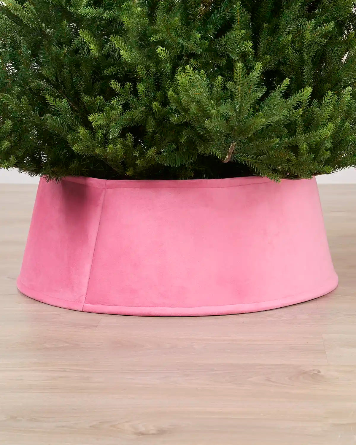 Velvet Pink tree collar around the base of a green Christmas tree placed on a light brown wooden floor
