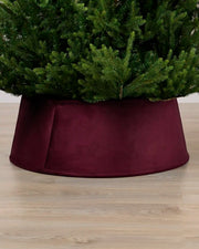 Velvet burgundy tree collar around the base of a green Christmas tree placed on a light brown wooden floor