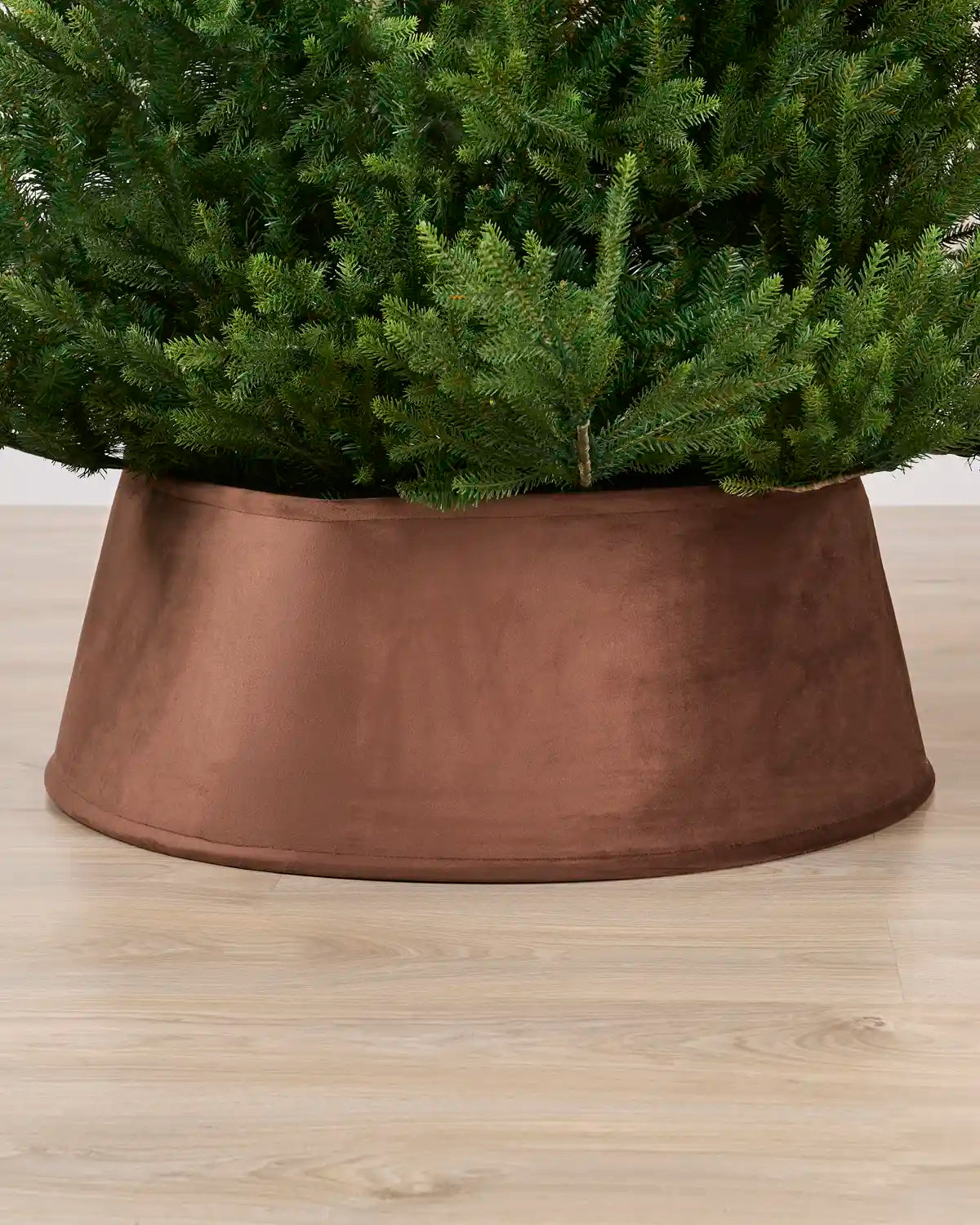 Velvet espresso tree collar around the base of a green Christmas tree placed on a light brown wooden floor
