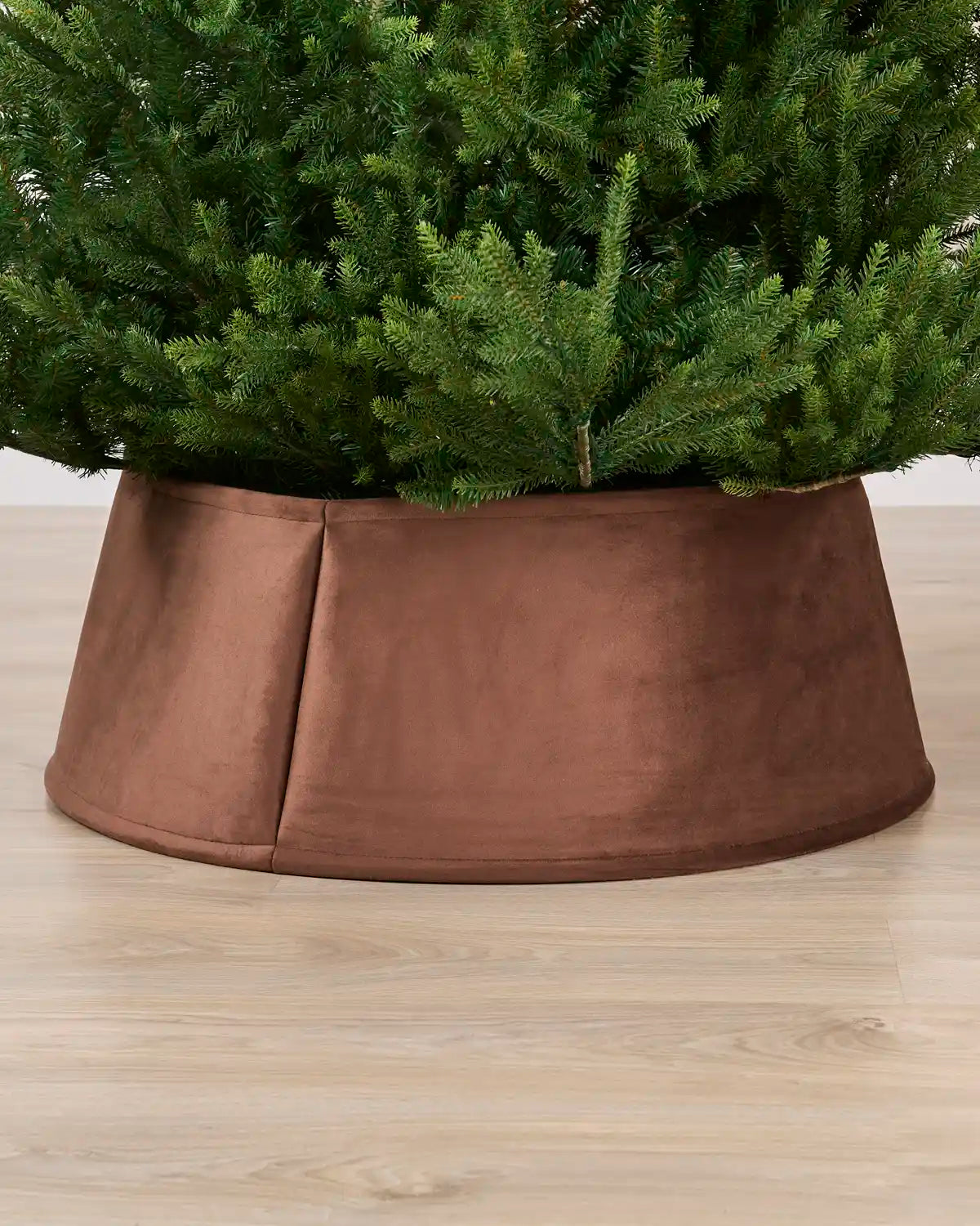 Velvet espresso tree collar around the base of a green Christmas tree placed on a light brown wooden floor
