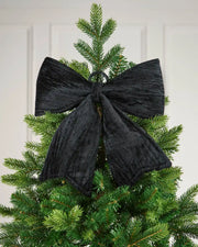 Vintage-style black velvet bow attached to top of Christmas tree in front of white background
