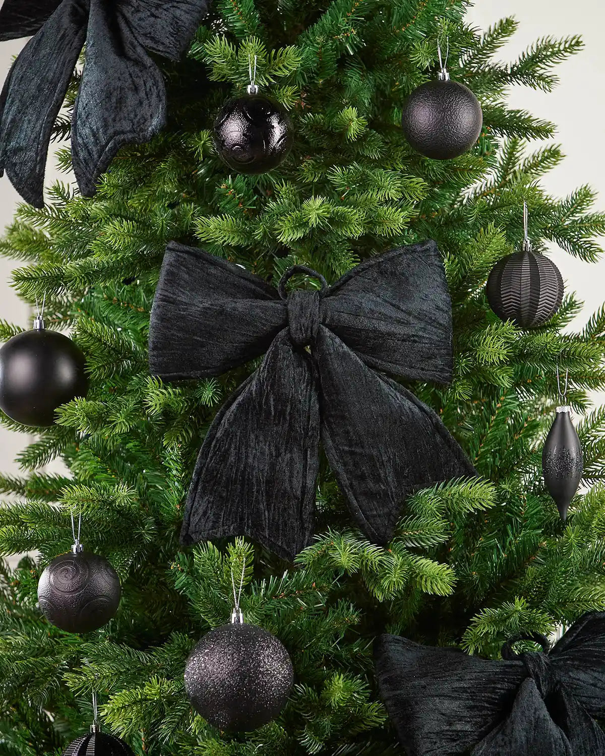 Vintage-style black velvet bow attached to Christmas tree surrounded by additional bows and black baubles
