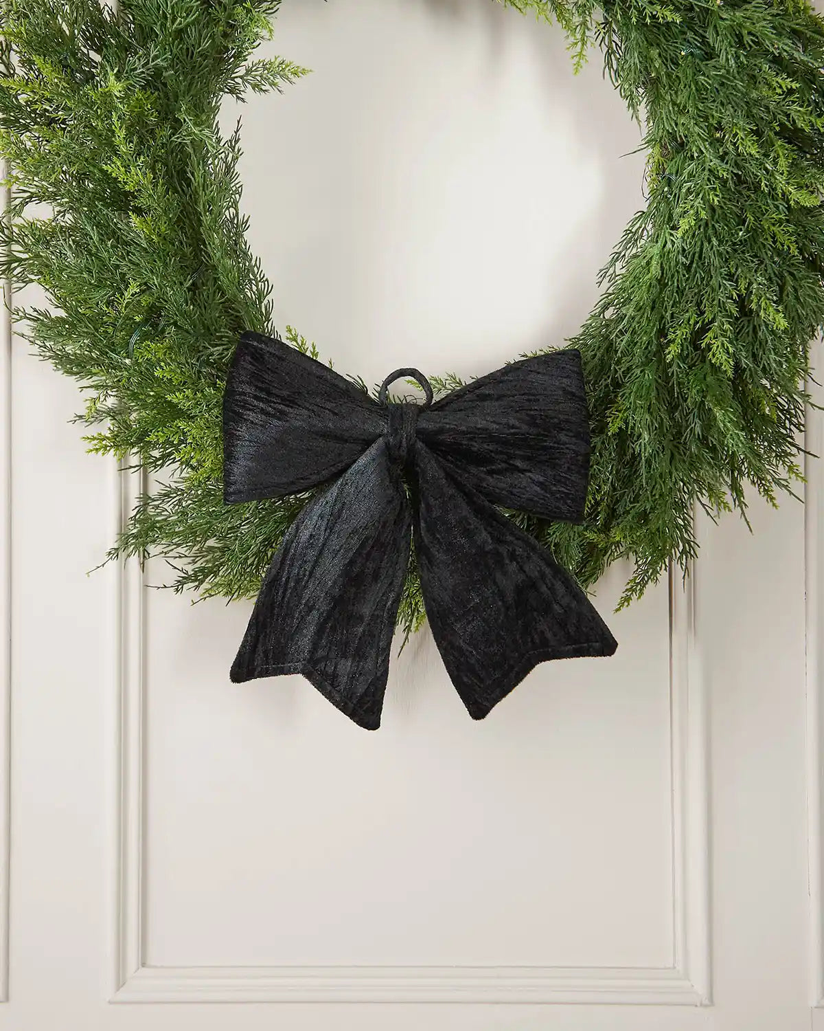 Vintage-style black velvet bow attached to wreath in front of white panel background