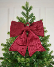 Vintage-style burgundy velvet bow placed near the top of a Christmas tree in front of a white background