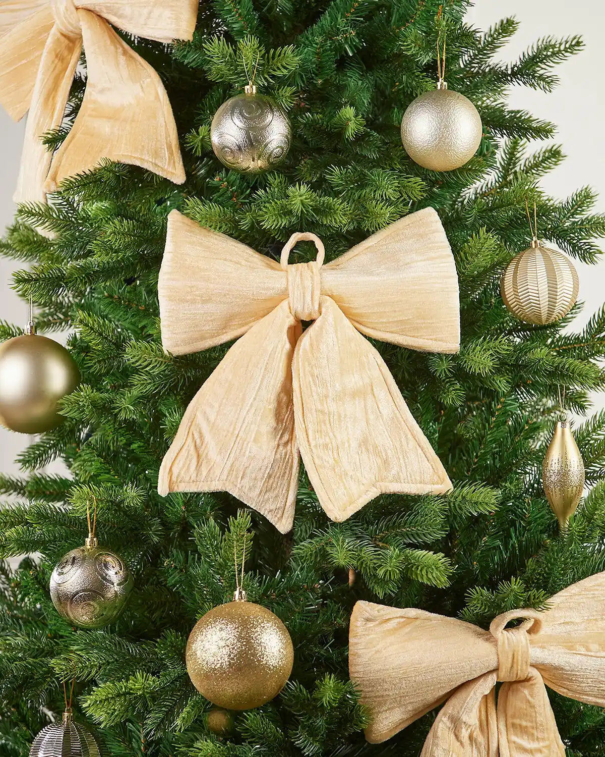 Vintage-style gold velvet bow attached to Christmas tree surrounded by additional bows and gold baubles