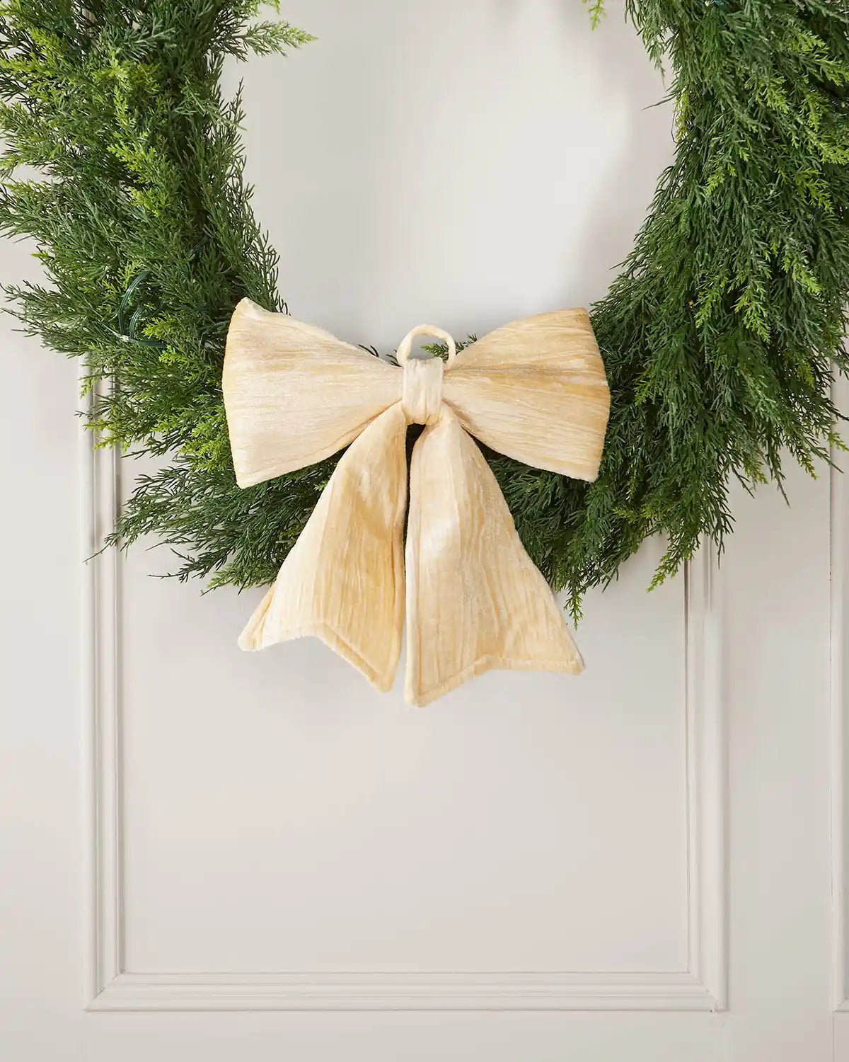 Vintage-style gold velvet bow attached to bottom of a wreath on a white background