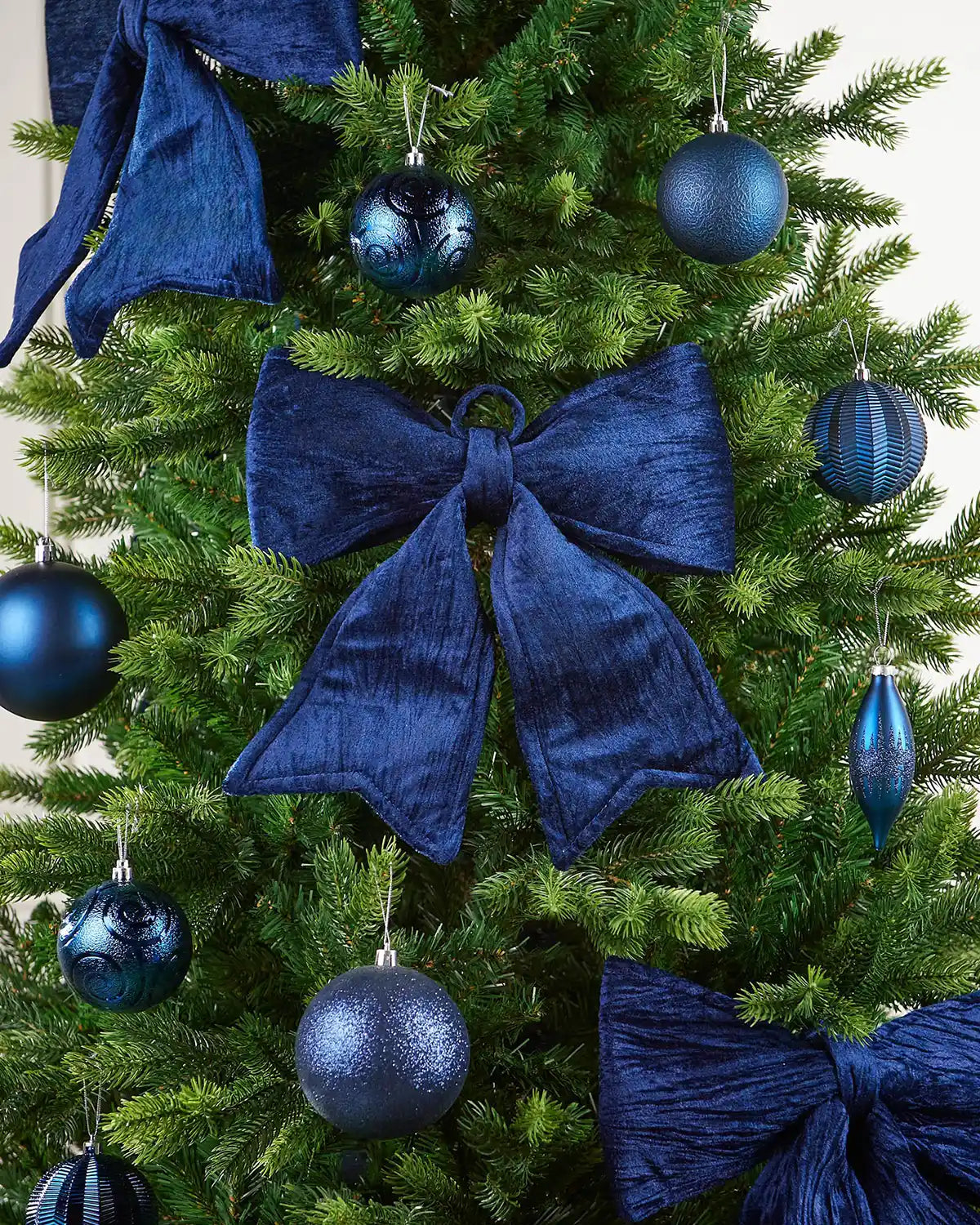 Close-up of vintage-style navy blue bow on Christmas tree surrounded by additional bows and navy blue baubles