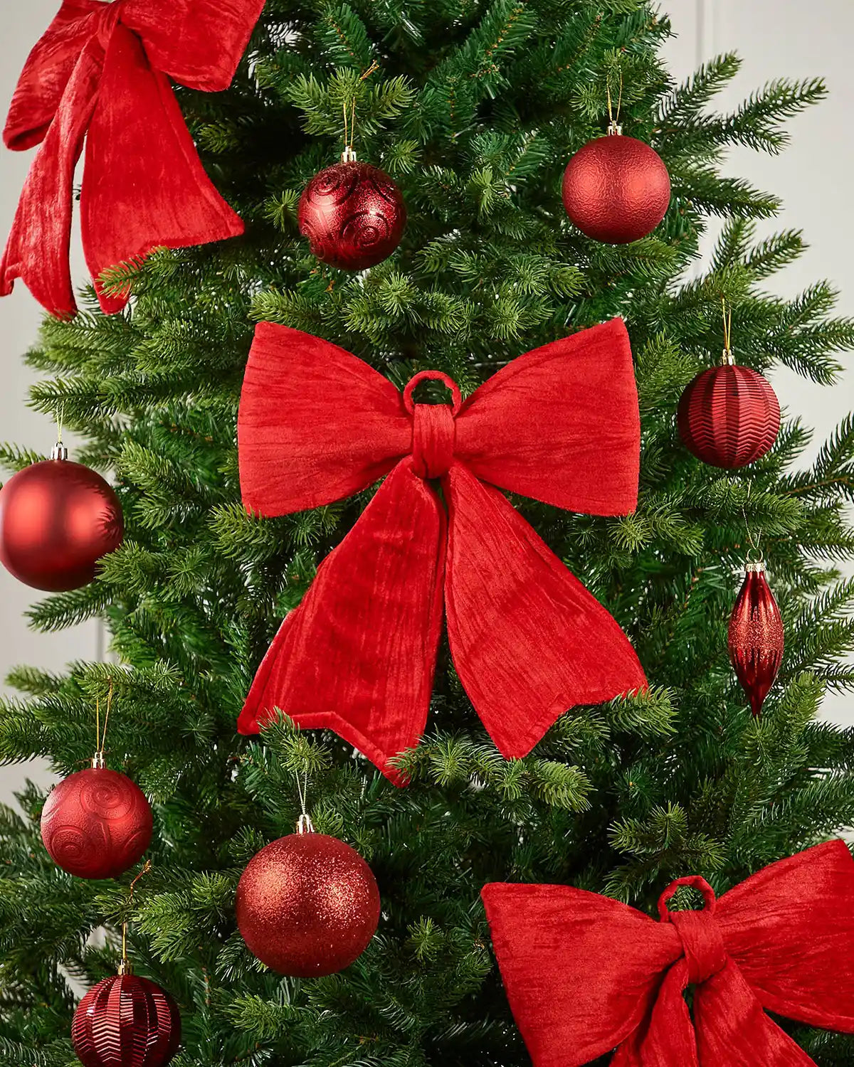Vintage-style red velvet bow attached to a Christmas tree surrounded by red baubles 