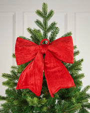 Vintage-style red velvet bow pinned near the top of a Christmas tree, in front of a white background