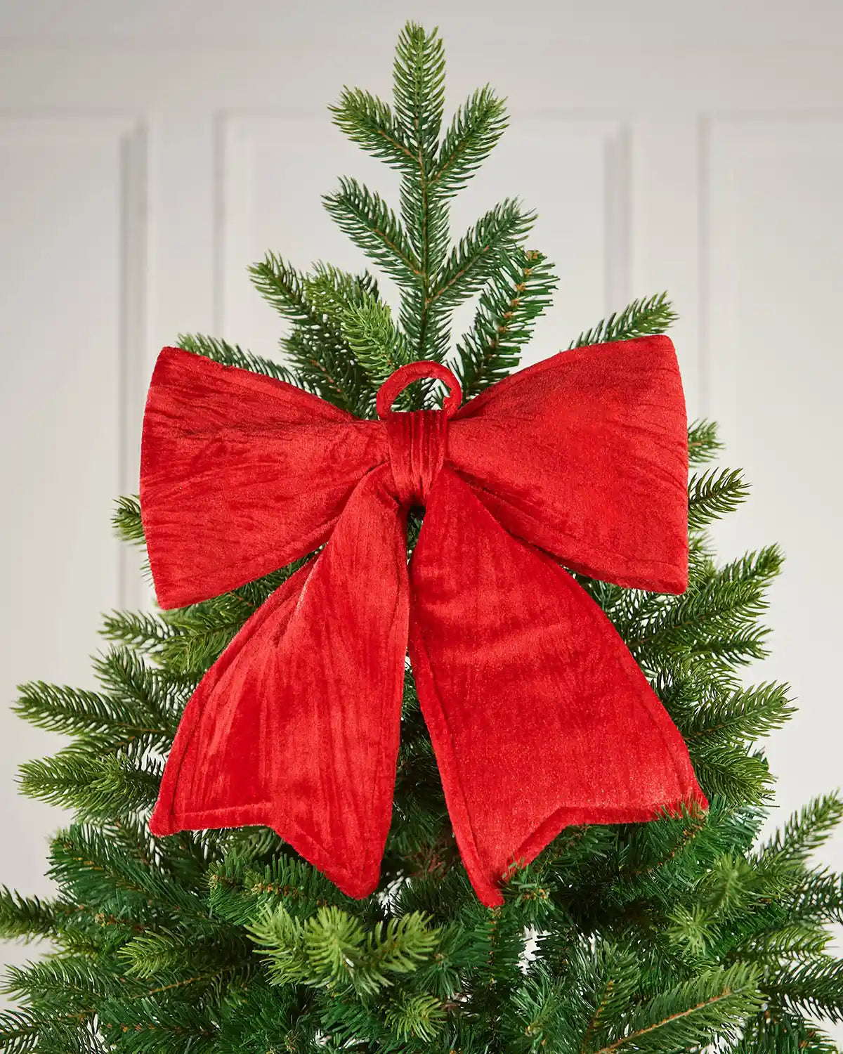 Vintage-style red velvet bow pinned near the top of a Christmas tree, in front of a white background