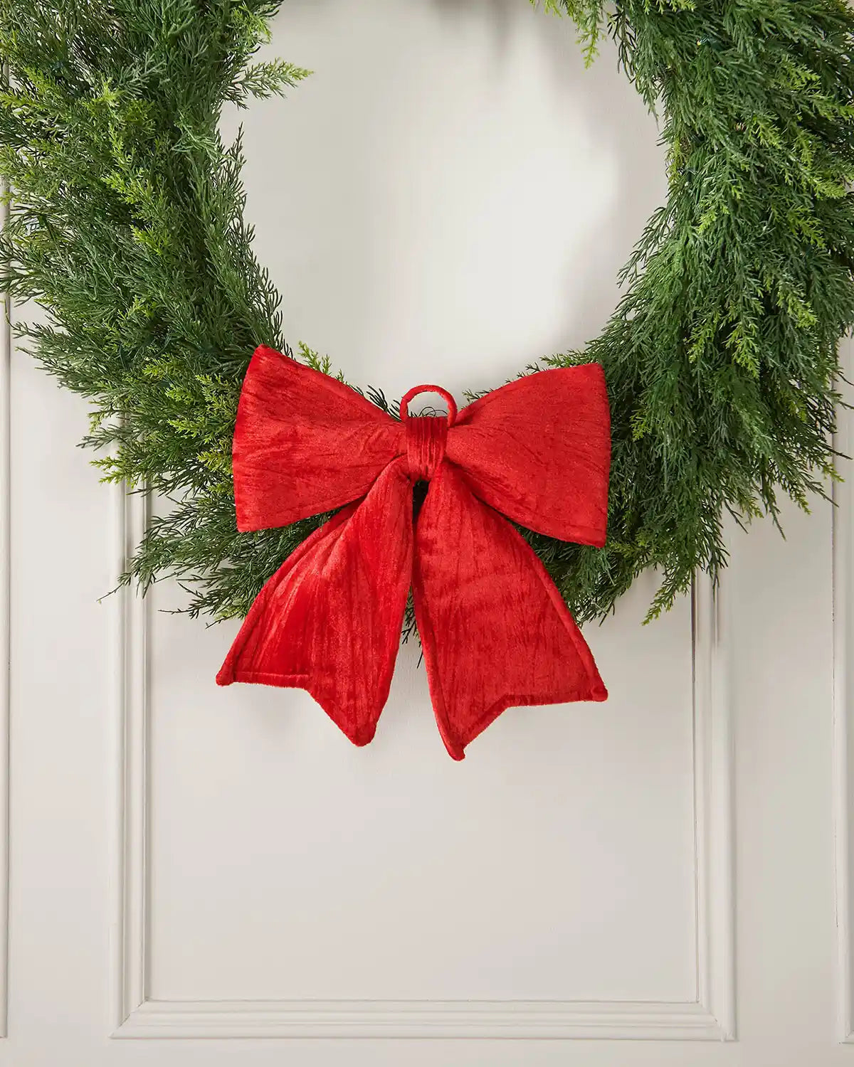 Vintage-style red velvet bow pinned to a green wreath which is almost fully in the picture