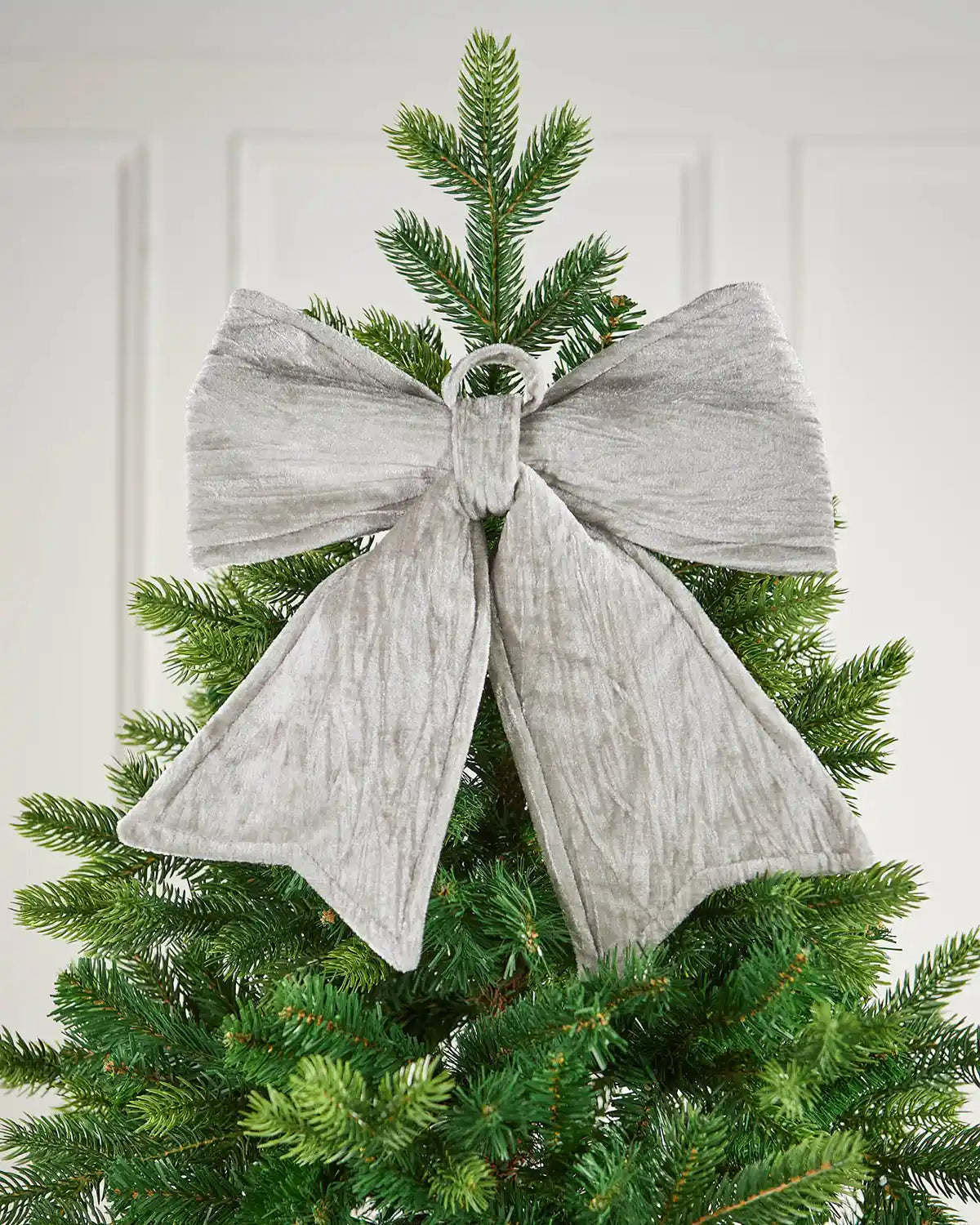 Vintage-style velvet bow attached near the top of the Christmas tree in front of a white background