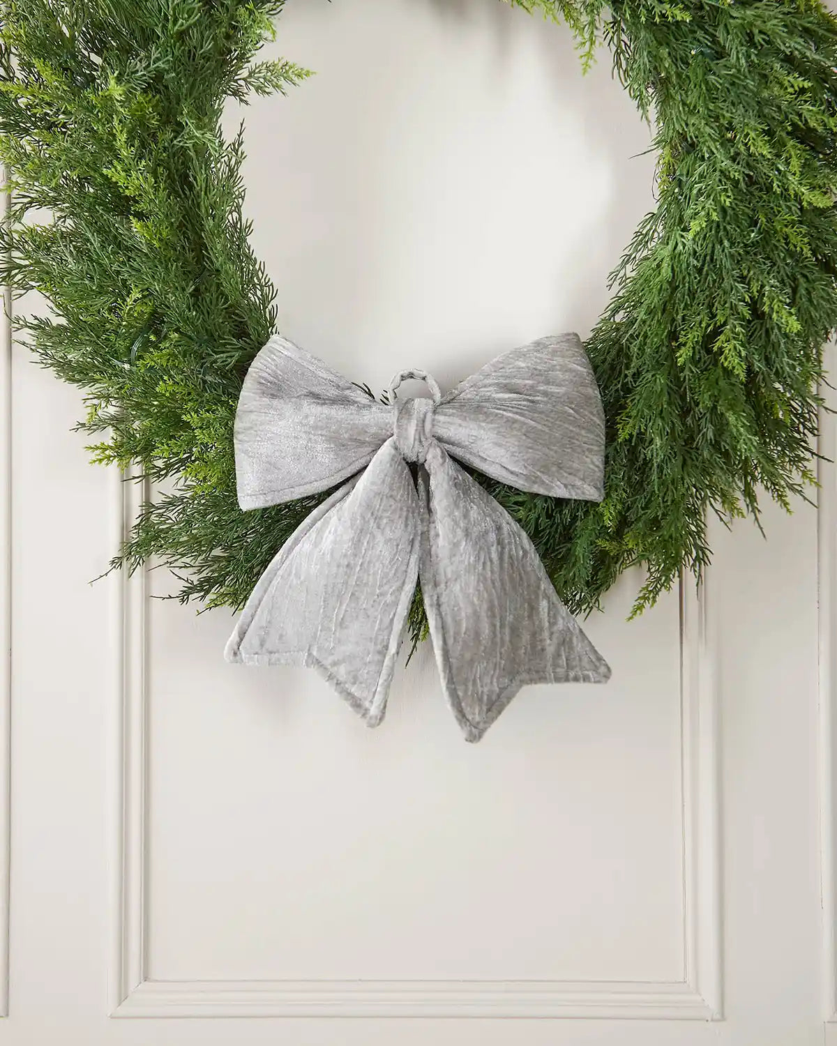 Vintage-style silver velvet bow attached to the bottom of a wreath in front of a white background
