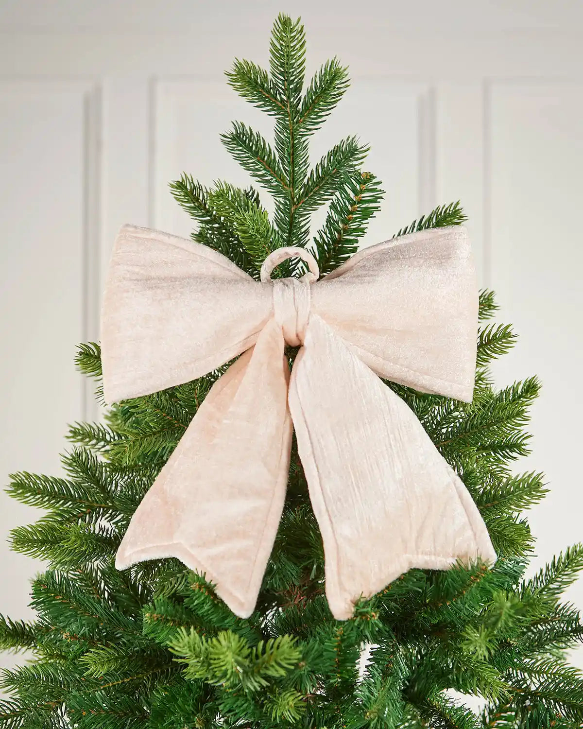 Vintage-style cream velvet Christmas bow attached to the top of a tree in front of white panelling