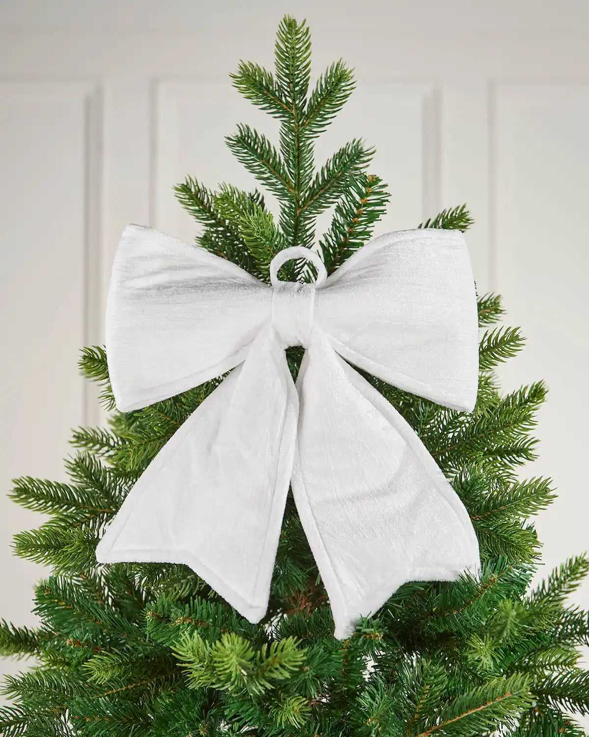 Vintage-style white velvet bow attached near the top of a Christmas tree in front of a white background