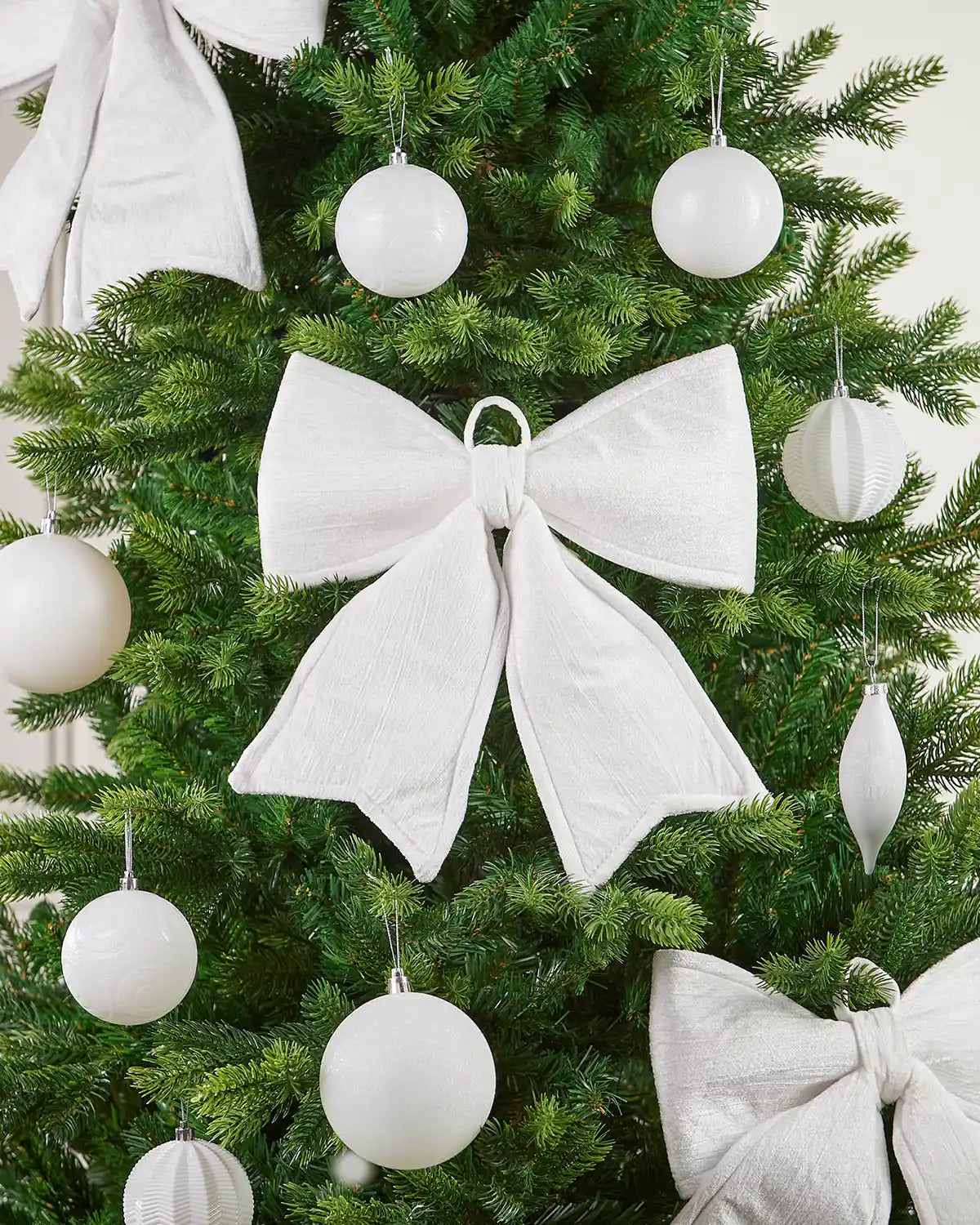 Close-up of vintage-style white velvet bow on Christmas tree surrounded by additional bows and white baubles