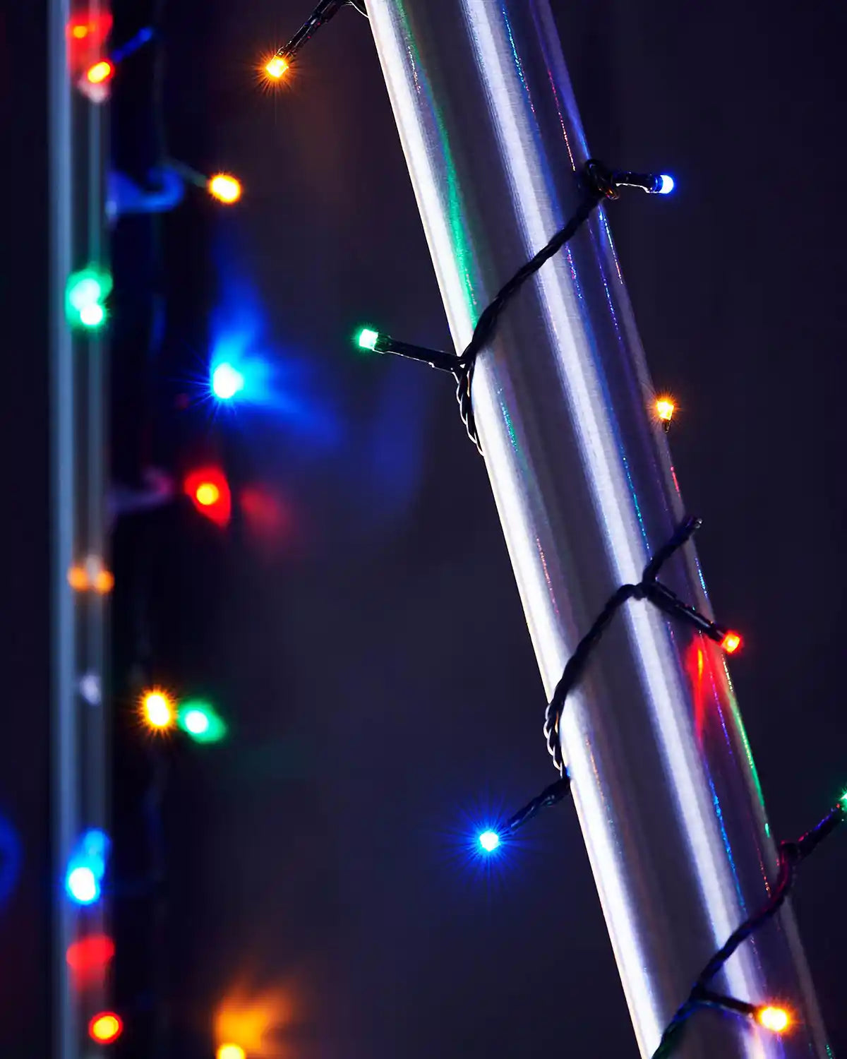 Multi-coloured string lights wrapped around an outdoor umbrella pole against a dark background
