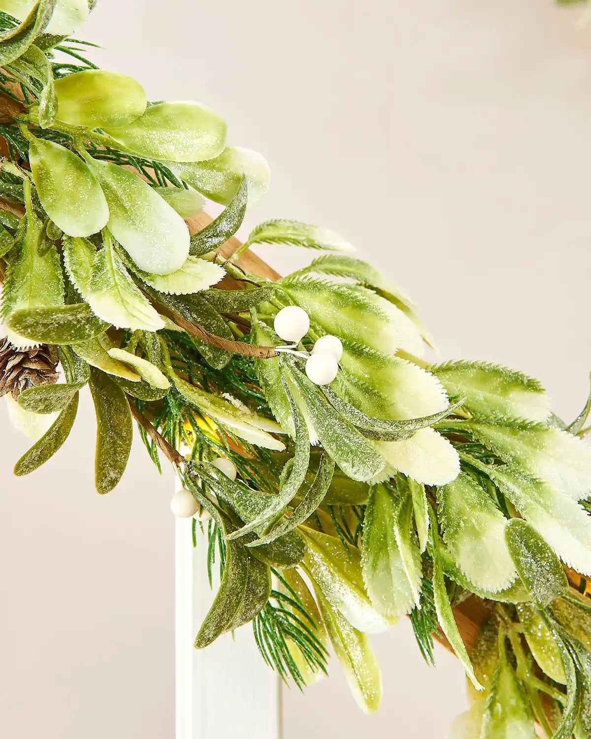 Close-up of a green wreath with mistletoe and white berries against a beige background