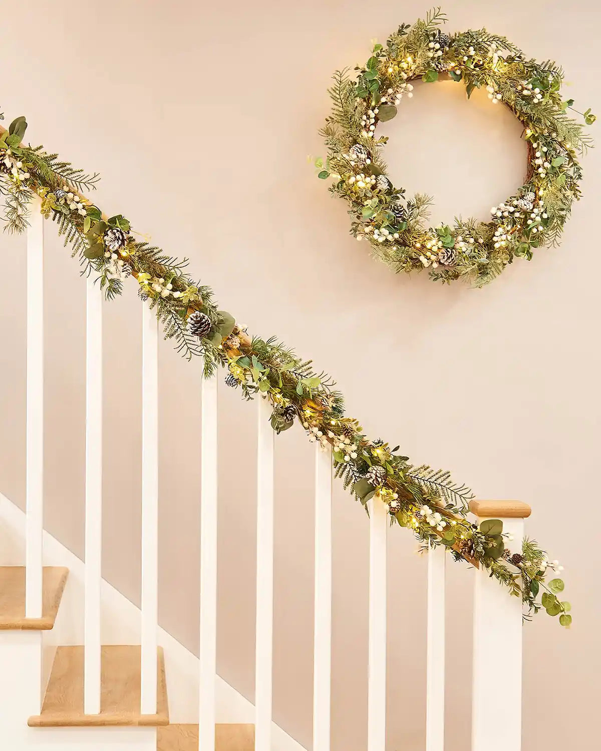 Decorative green wreath and garland with White berries, pinecones and lights on a staircase banister with a neutral background