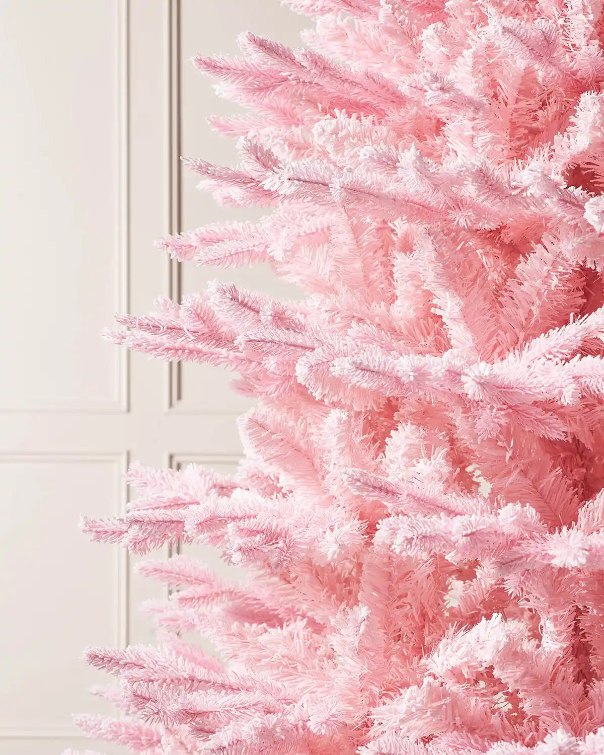 Close-up of a pink artificial Christmas tree against a cream wall.