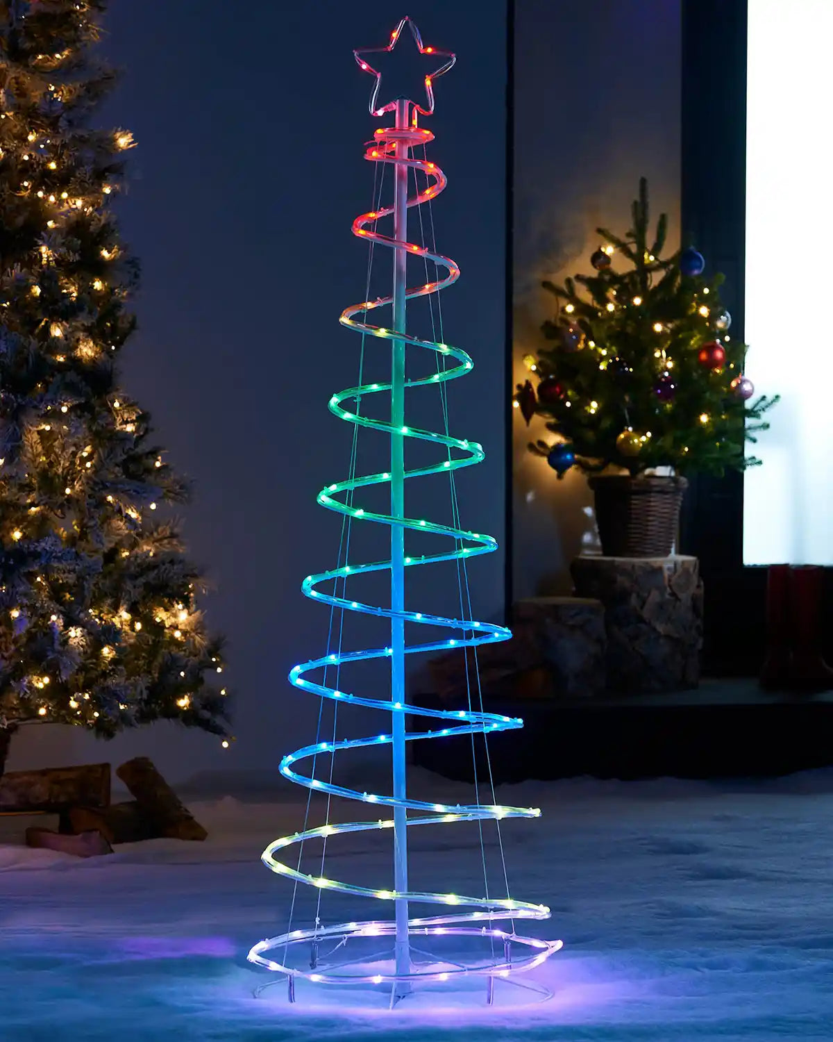 Colorful LED spiral tree in a snowy outdoor setting with Christmas trees in the background.