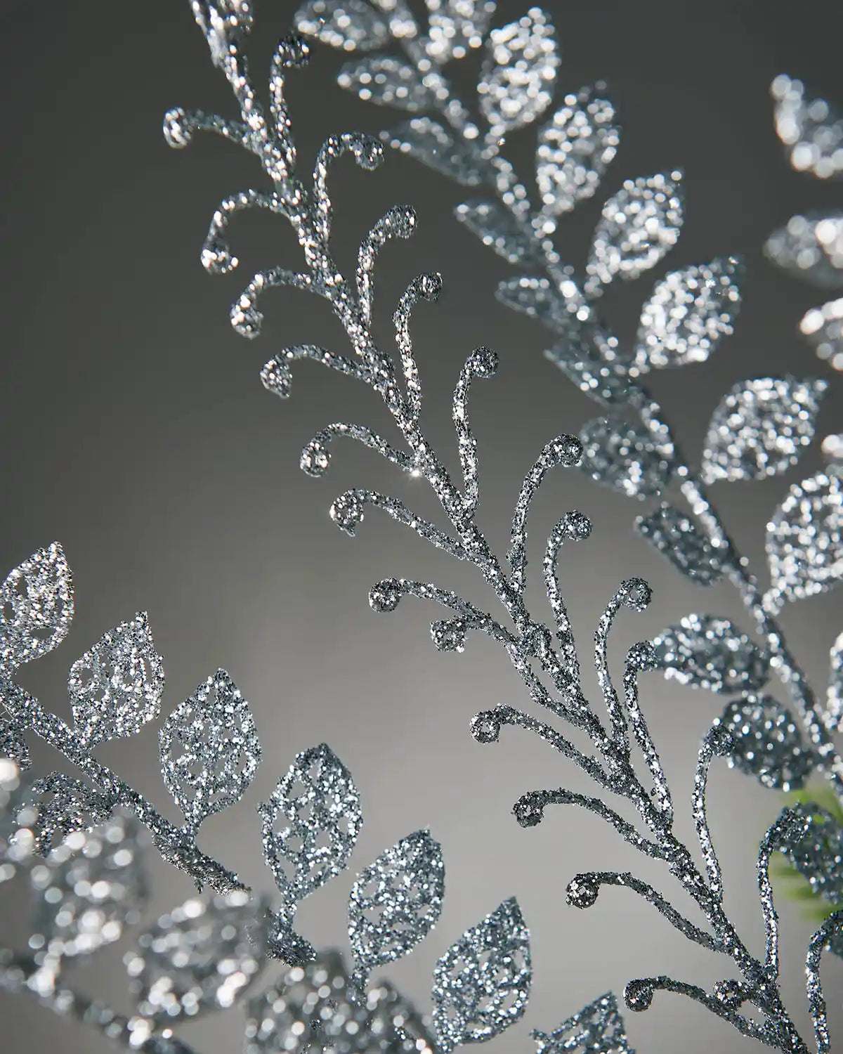 Decorative silver glitter leaf spray with etched leaf patterns on a dark background