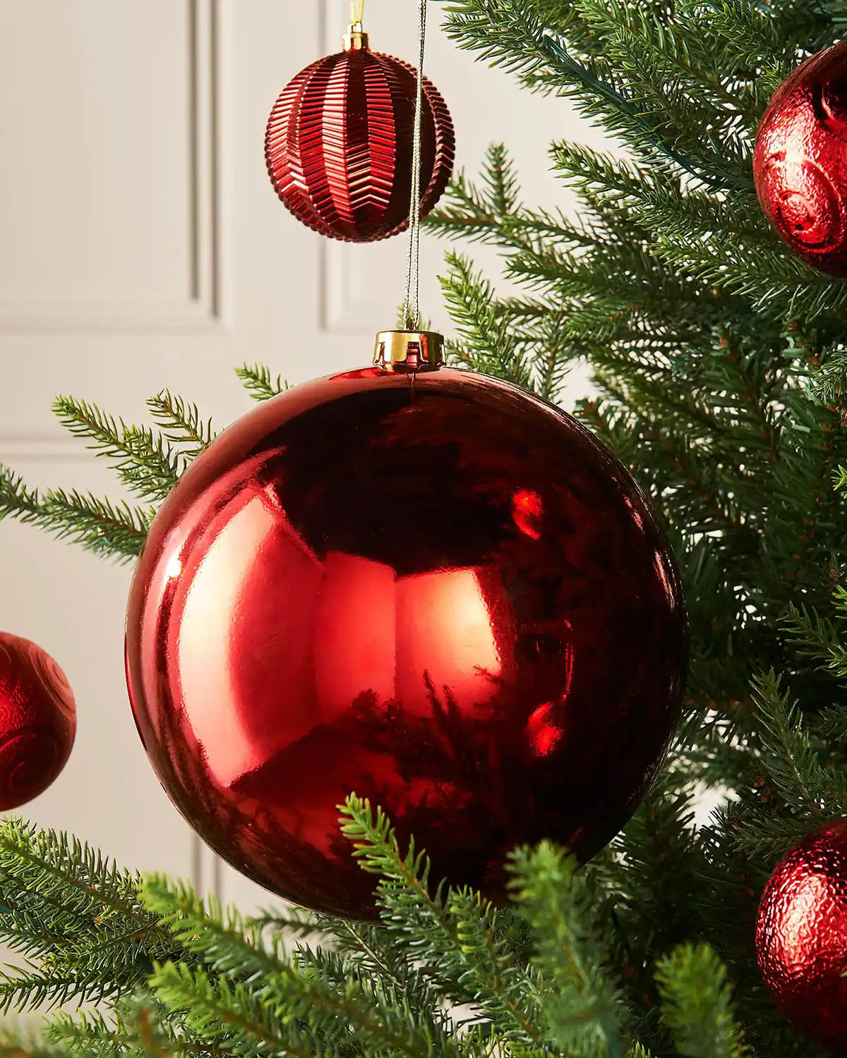 Large oversized Red gloss bauble on the middle of a Christmas tree branch accompanied by a 4 smaller red textured baubles