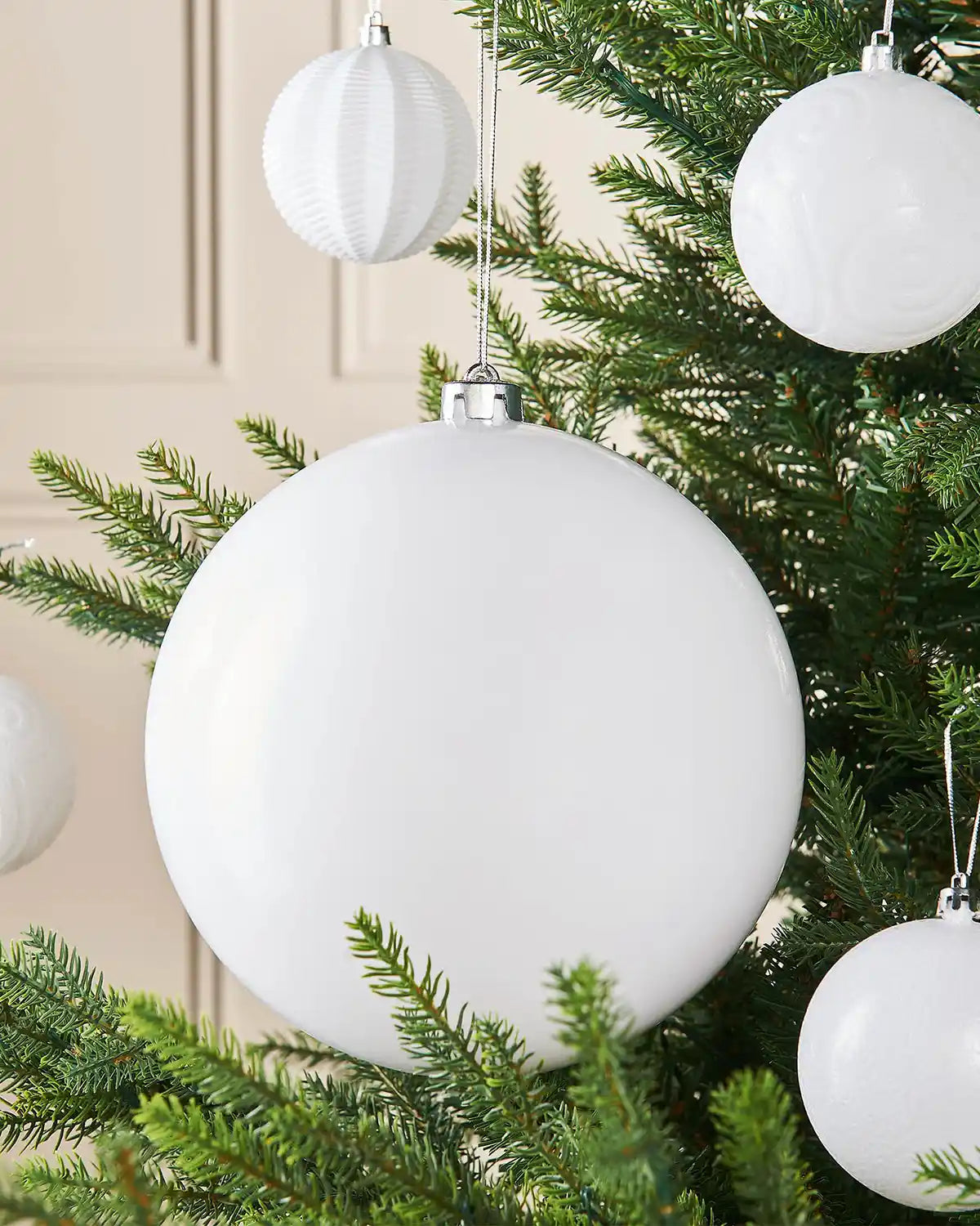 White oversized gloss bauble on a Christmas tree accompanied by 4 smaller white baubles