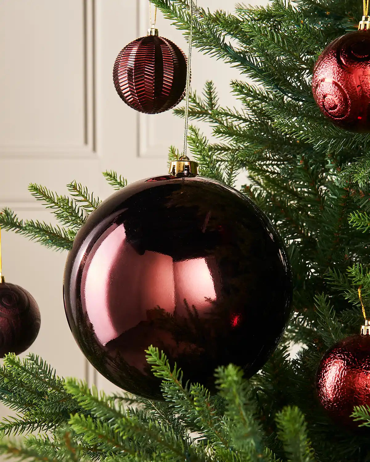 Gloss oversized burgundy bauble on a Christmas tree branch with 4 smaller burgundy baubles in the background