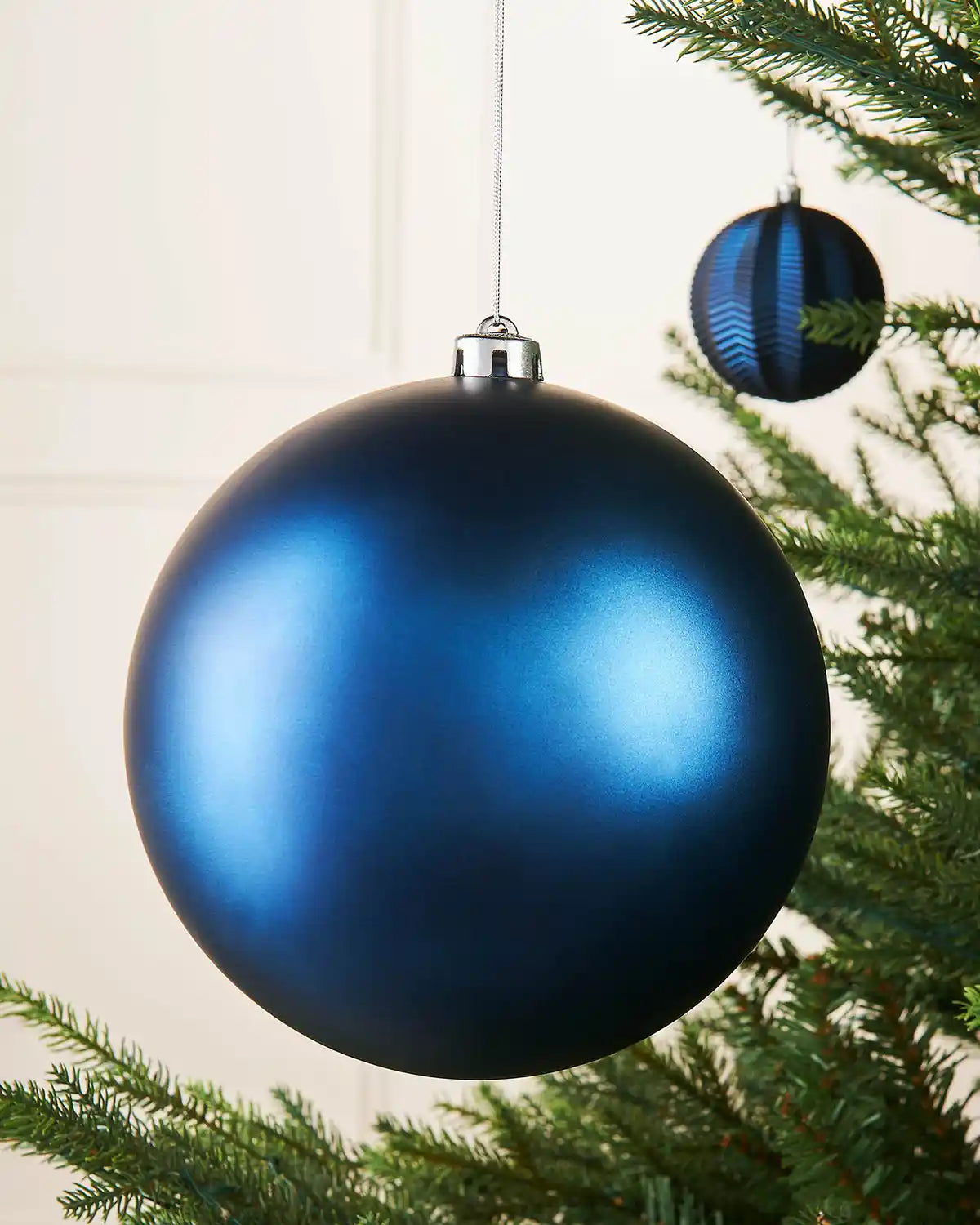 Navy blue oversized bauble on a Christmas tree branch with a smaller blue bauble in the background