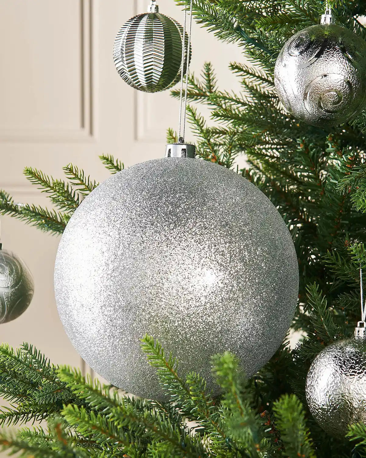 Silver glittery Christmas bauble hanging on a tree branch with 4 smaller silver baubles in background