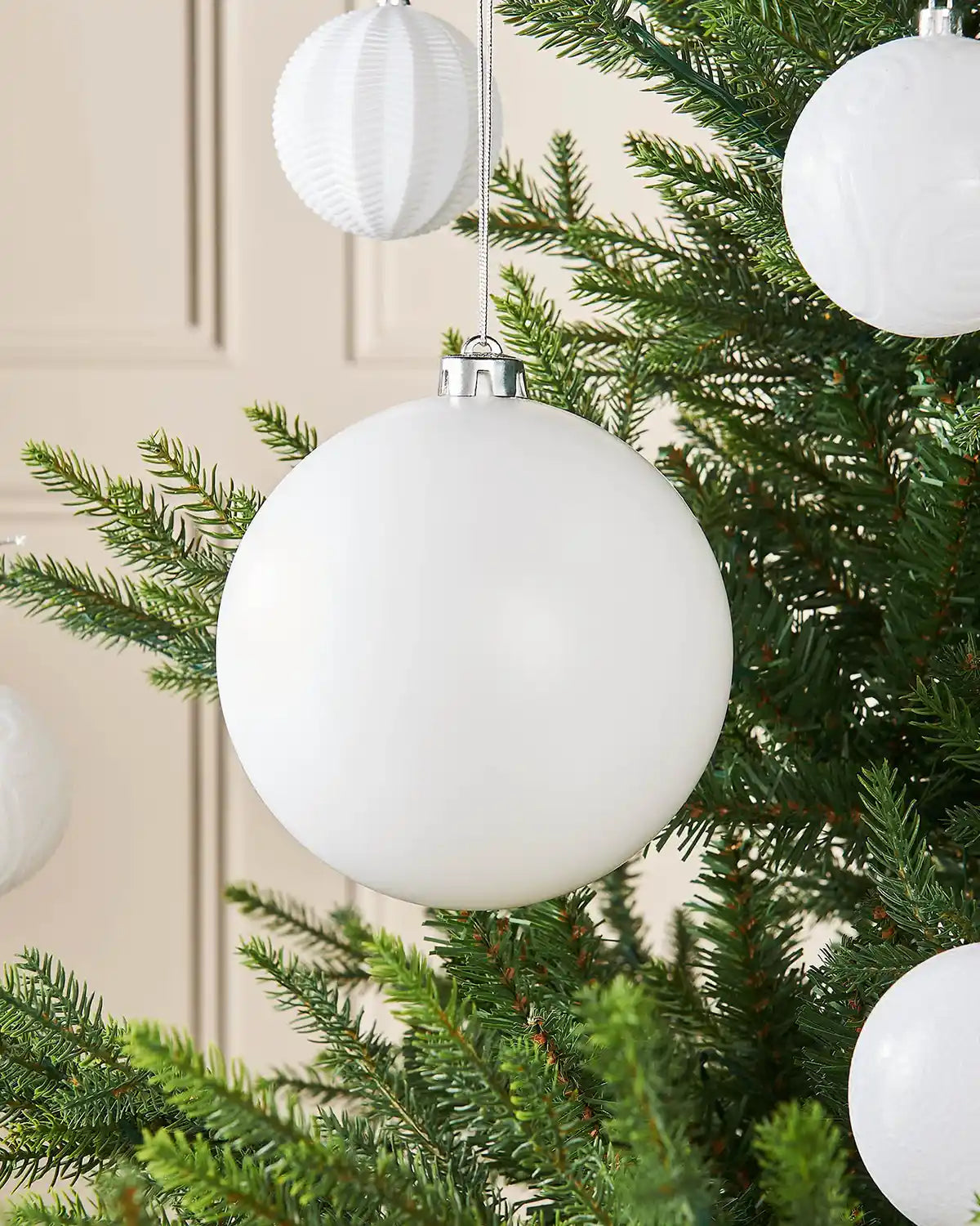 Matt white 15cm oversized bauble on a Christmas tree branch with 4 smaller white baubles in background