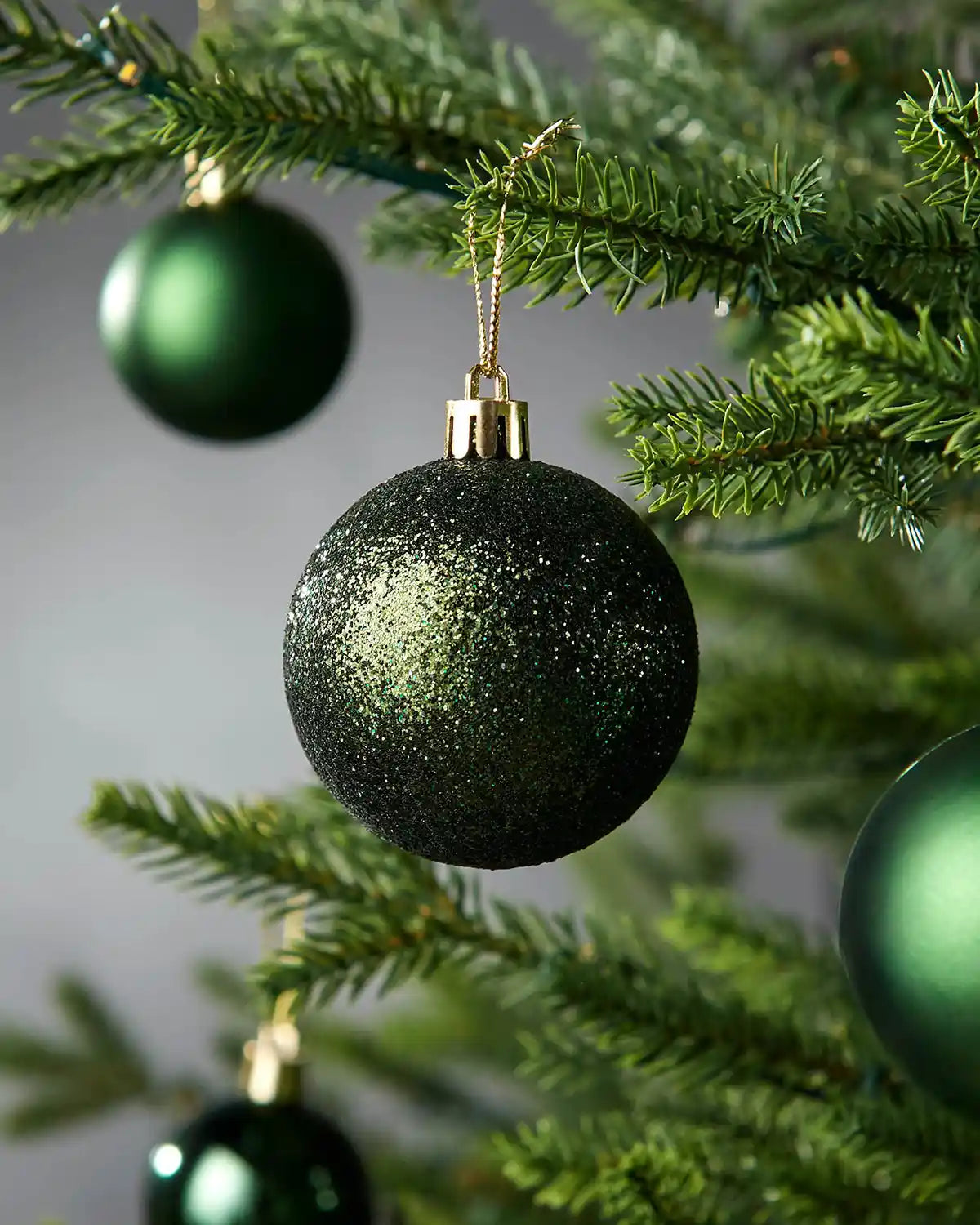 Green glittery Christmas baubles on a tree branch with a blurred background
