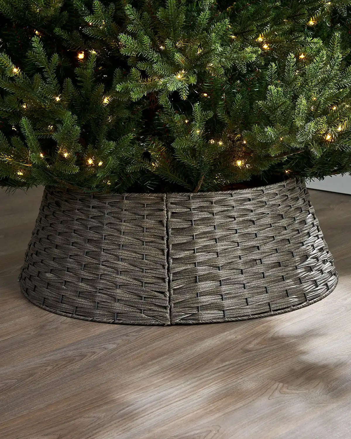 Grey Wicker Christmas tree collar around a decorated Christmas tree on a wooden floor.