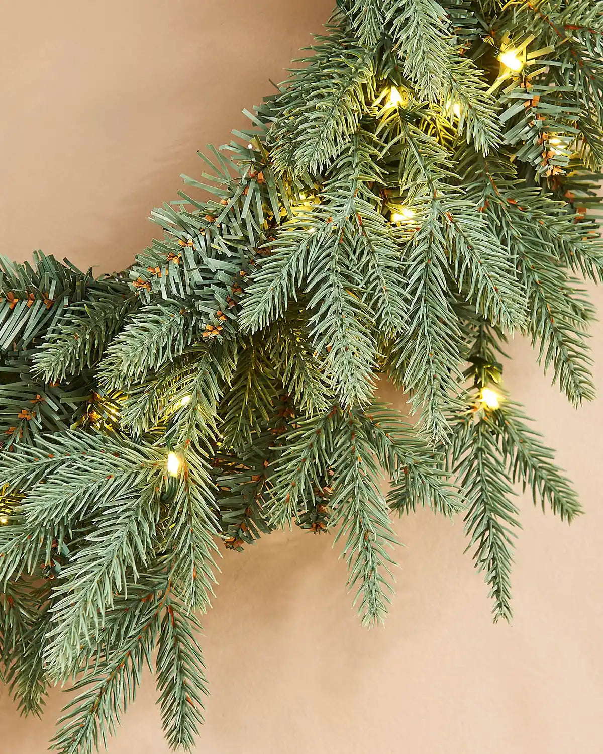 Close up of single lit bulbs on a  Blue Mixed Pine Wreath, 60 cm on a cream wall