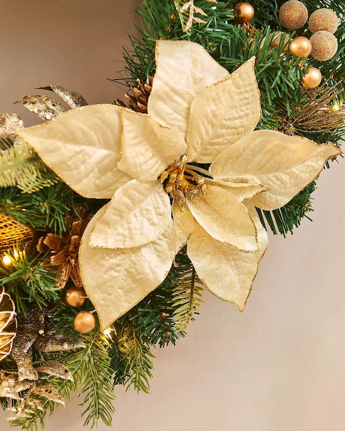 Close up of Decorative Christmas wreath with gold poinsettia and ornaments on a neutral background