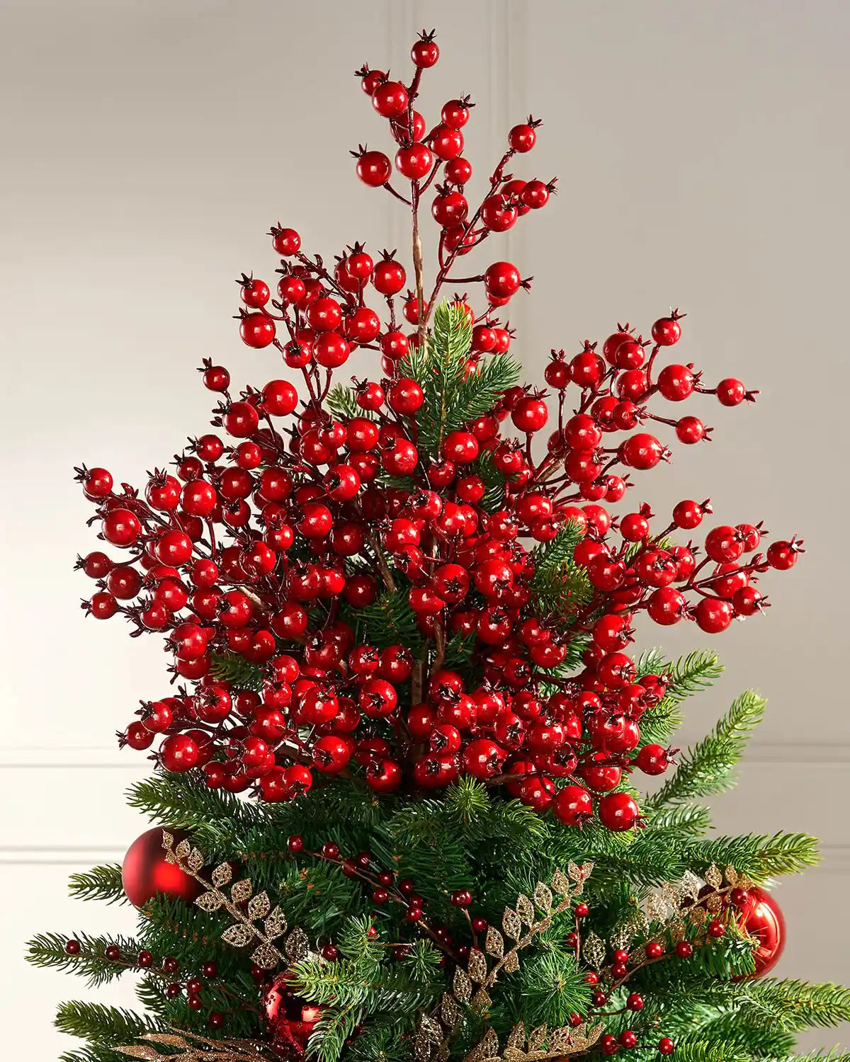 Decorative Christmas tree with red berries tree topper on a plain background