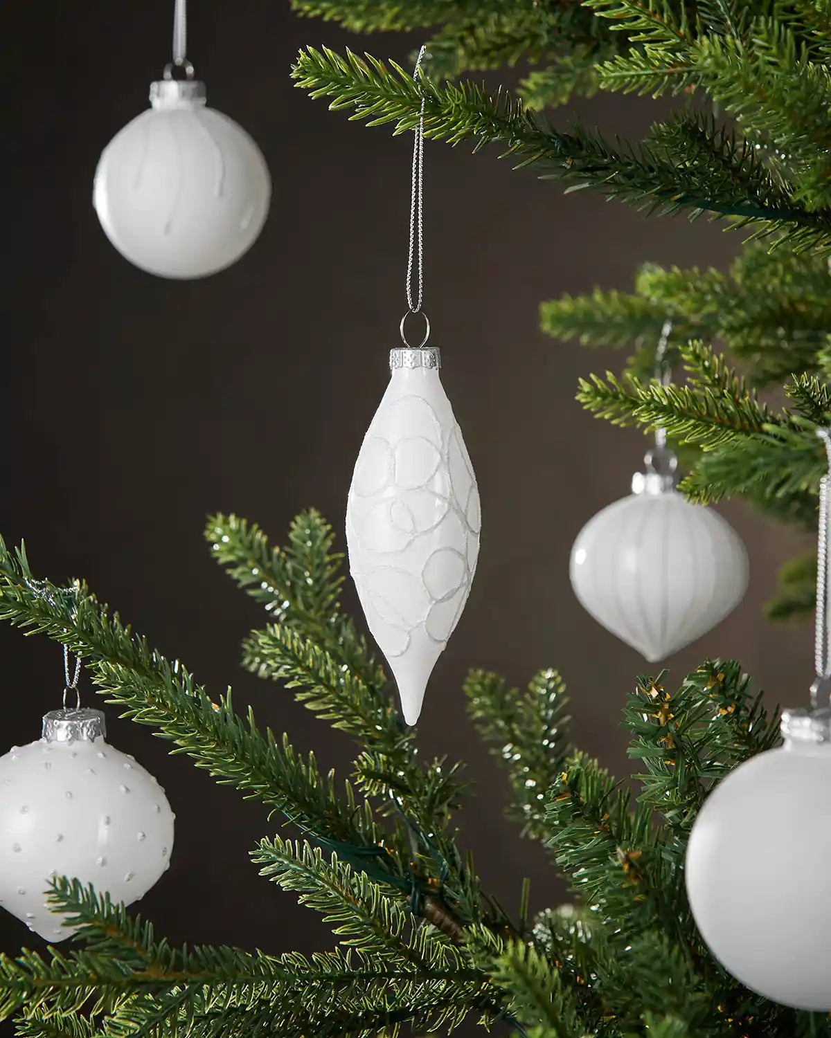 White textured Christmas baubles on a green tree against a dark background