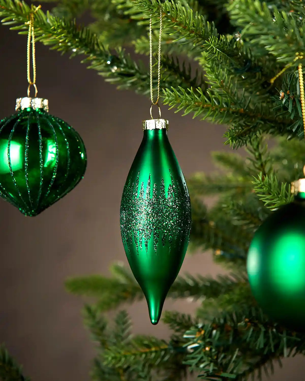 Three Green glass ornaments hanging on a Christmas tree with a plain background