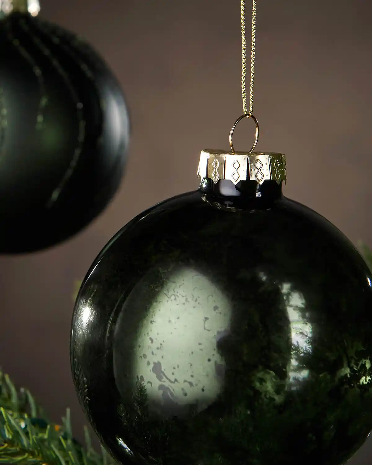 Close up of 2 sage green Christmas ornament hanging on a tree with a gold chain against a blurred background