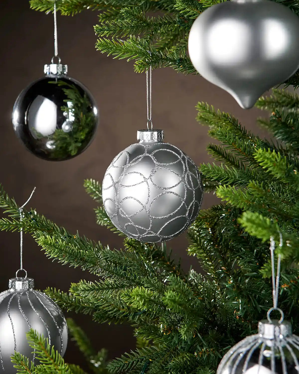 Five silver baubles hanging on a Christmas tree branch with a brown background 