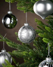 Five silver baubles hanging on a Christmas tree branch with a brown background 