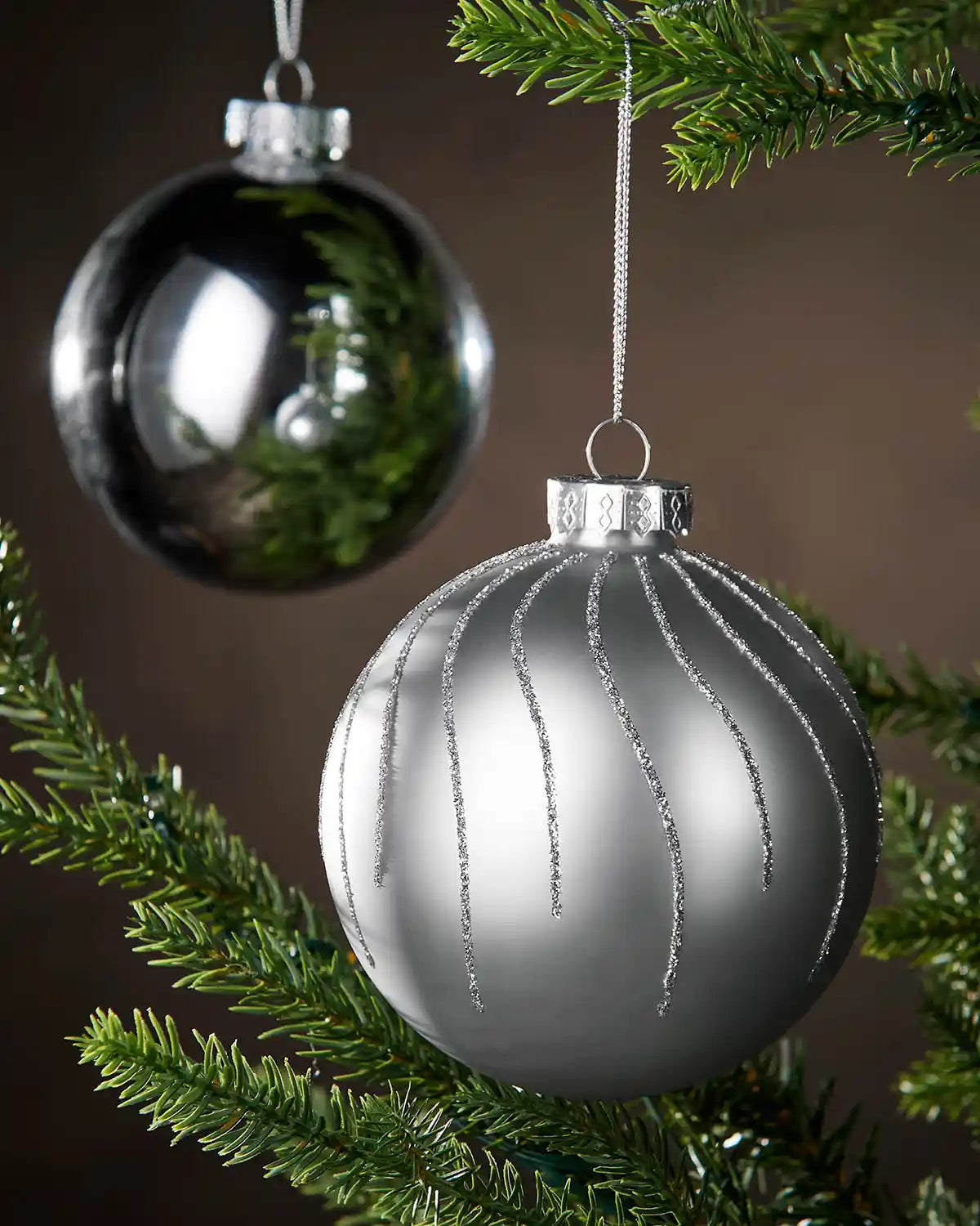 Close up 2 Silver Christmas ornament hanging on a tree branch with a dark background