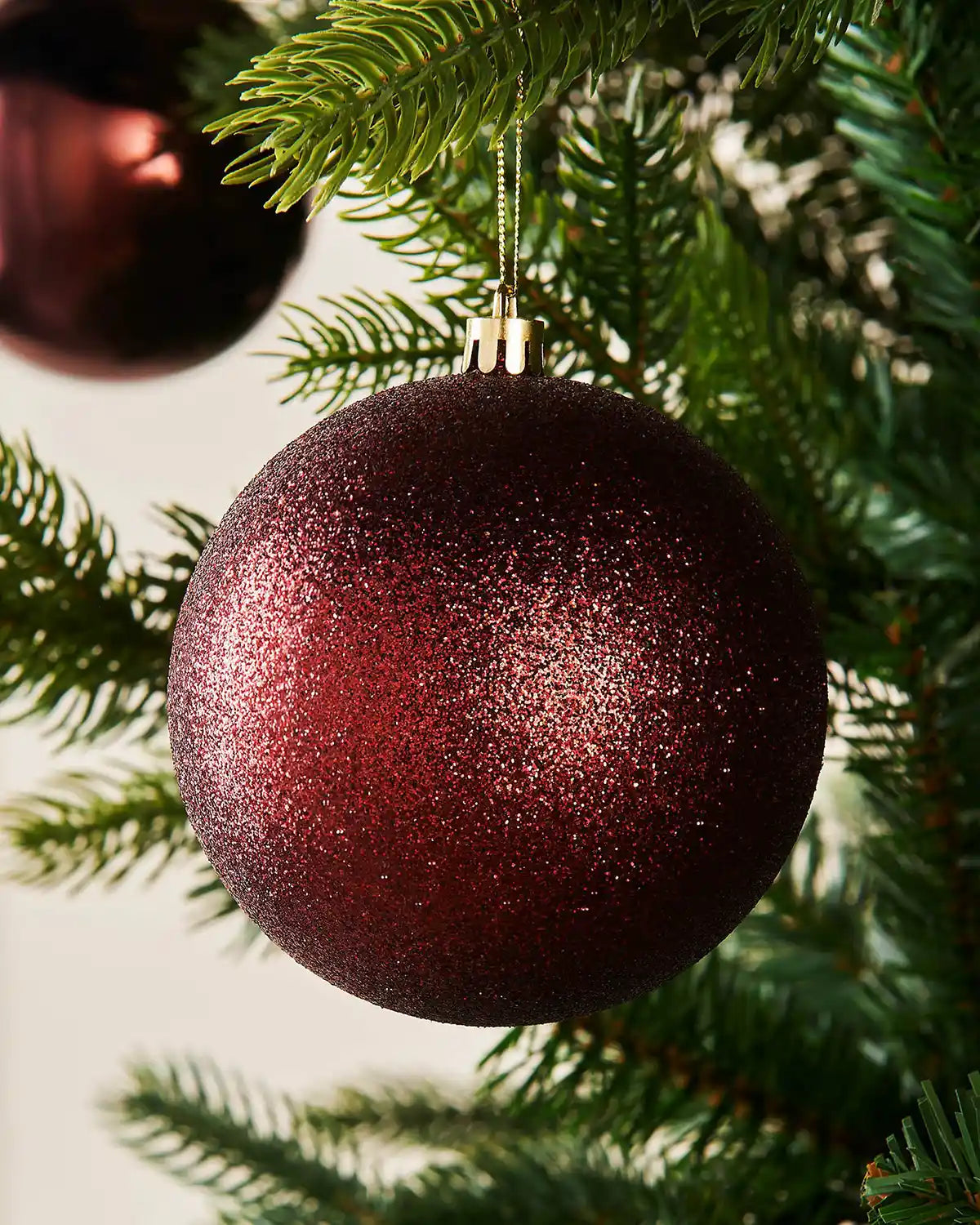 Burgundy glittery Christmas ornament hanging on a tree branch