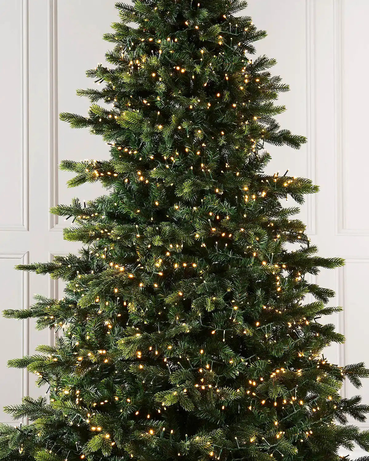 Decorated Christmas tree with warm cluster lights against a white wall