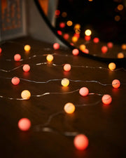 Orange and yellow berry shape string lights on a wooden table with a mirror in the background
