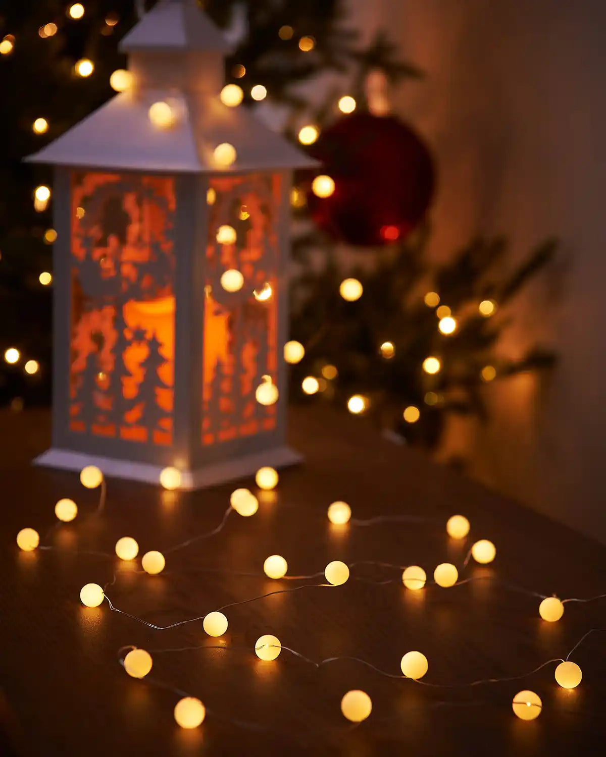 Decorative lantern with cut-out designs illuminated by warm white string lights on a wooden surface.